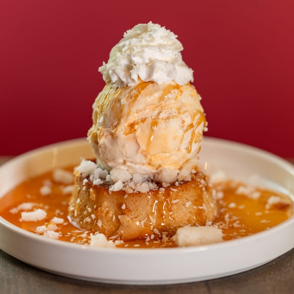 Flan dessert topped with vanilla ice cream, whipped cream, caramel, and shredded coconut.