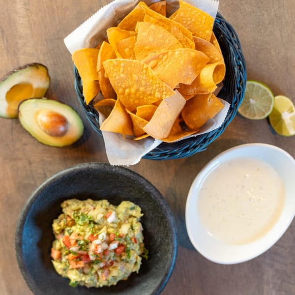 Dahlia's tortilla chips, guacamole, and queso dip, with avocado halves and lime wedges.