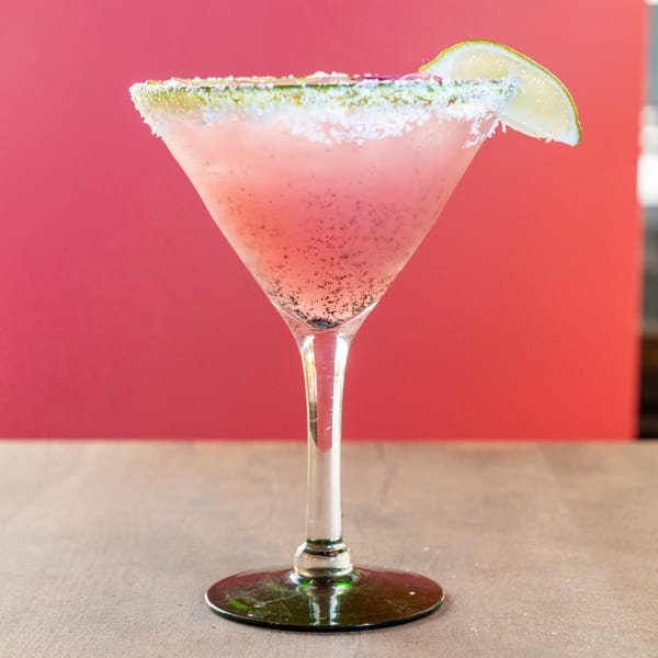 Pink Dahlia margarita with a salted rim and lime wedge, against a vibrant red background.